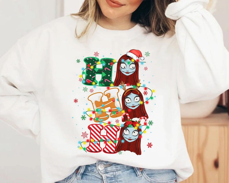 Peut inclure: Sweat-shirt blanc avec un motif de No&euml;l. Le texte "HO HO HO" est compos&eacute; d'&eacute;l&eacute;ments festifs : vert avec des lumi&egrave;res, pain d'&eacute;pices et rayures rouges et blanches. Sally de L'&Eacute;trange No&euml;l de Monsieur Jack est repr&eacute;sent&eacute;e.