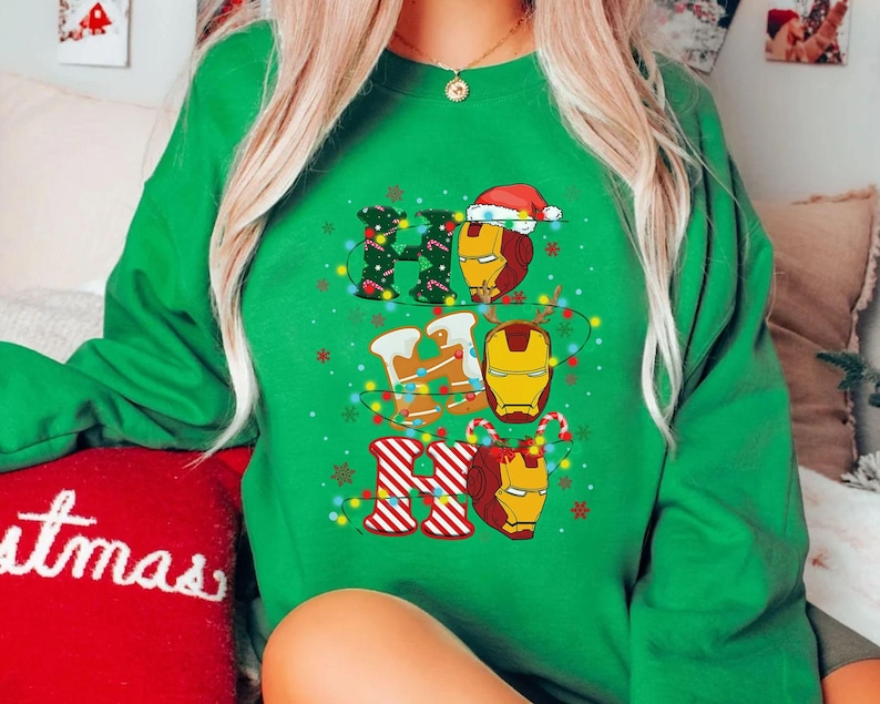 May include: Green sweatshirt with a festive "Ho Ho Ho" design. The design features Iron Man's helmet incorporated into the letters, with Christmas lights and a Santa hat. The sweatshirt is a vibrant green color.