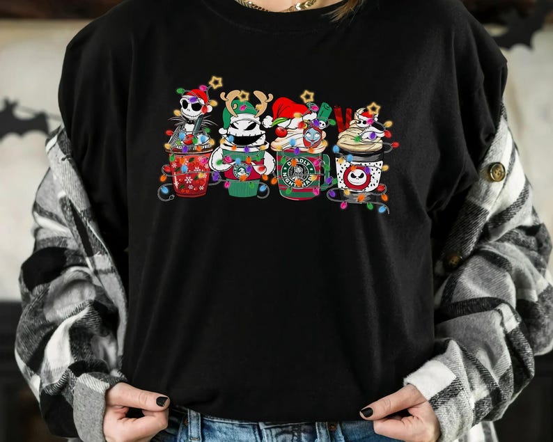 May include: Black crew neck t-shirt featuring four cartoon coffee cups decorated with Christmas lights and characters from The Nightmare Before Christmas. The cups have different designs and colors, including Jack Skellington and Zero.