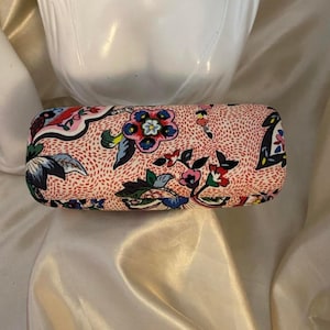May include: A rectangular hard-shell glasses case featuring a light pink background with a dense pattern of small red dashes. The surface is decorated with large, colorful floral motifs in shades of blue, green, red, and white throughout.