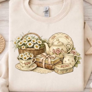 May include: Cream-colored sweatshirt featuring a floral still life design. The illustration includes a basket of daisies, a teacup and saucer, a teapot, books, and a small decorative box. The design is in soft pastel colors.