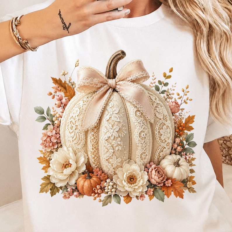 Floral lace pumpkin PNG displayed on a clean white t-shirt mockup. The fall design includes a large cream pumpkin with lace border detailing, elegant floral lace panels, a soft blush bow, ivory flowers, pink blossoms, orange fall leaves, berries, sage greenery, and mini pumpkin accents. Great for coquette fall shirt designs, lace pumpkin PNG listings, pumpkin bow PNG art, autumn PNG design files, pumpkin patch shirts, boutique fall graphics, and trendy fall sublimation projects.