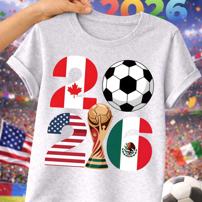 World Soccer Cup 2026 soccer PNG displayed on a light gray t-shirt mockup with a stadium background, featuring bold 2026 typography filled with USA, Canada, and Mexico flag designs, a soccer ball icon, and a gold trophy illustration. This high-quality transparent PNG is ideal for print on demand t-shirts, kids soccer shirts, fan apparel, sublimation projects, and football merchandise celebrating the 2026 world soccer tournament.