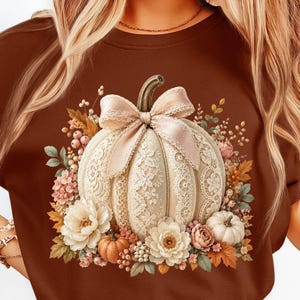 Coquette lace pumpkin PNG displayed on a warm brown fall t-shirt mockup. The artwork features an elegant cream pumpkin with lace border panels, a soft bow, floral lace texture, blush flowers, ivory blooms, orange leaves, berries, greenery, and mini pumpkins. Perfect for fall pumpkin shirt designs, lace pumpkin shirt graphics, pumpkin patch apparel, boutique fall PNG projects, preppy fall PNG listings, autumn sublimation designs, and trendy fall shirt mockups.