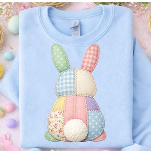 May include: A pale blue sweatshirt with a patchwork bunny motif. The bunny is crafted from pastel fabrics, such as polka dots, gingham, and floral prints. A fluffy white pom-pom forms the tail. Ideal for Easter celebrations, the sweatshirt is a charming garment.