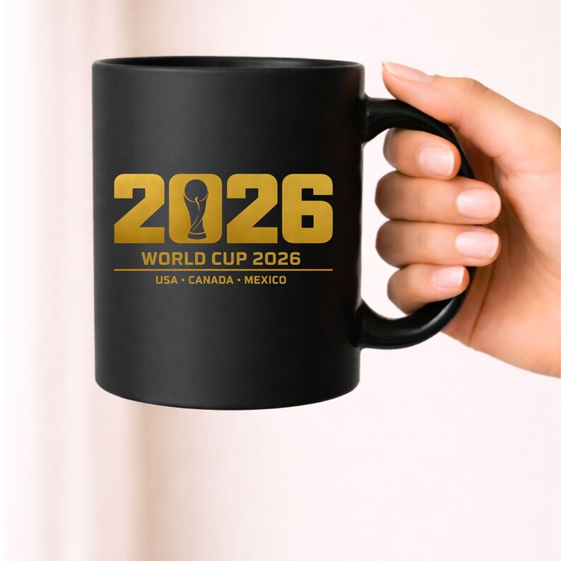 Black coffee mug mockup showing a gold soccer design featuring the year 2026 with a stylized trophy icon forming the zero and text reading World Cup 2026 USA Canada Mexico. This 2026 sports design is ideal for sublimation printing on mugs, tumblers and drinkware as well as apparel designs for soccer fans. Perfect digital graphic for print on demand sellers and Cricut creators producing sports themed merchandise.