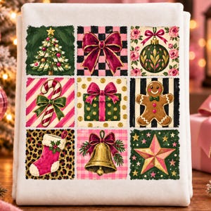May include: A white fabric towel featuring a grid of nine festive squares. The illustrations include a Christmas tree, a pink bow, a floral ornament, a candy cane, a green gift box, a gingerbread man, a pink stocking, a gold bell, and a star.