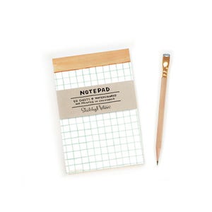 May include: A green grid notepad with a wooden top and a brown label that says "NOTEPAD 50 SHEETS WATERCOLORED AND PRINTED IN CALIFORNIA Sketchy Notes".