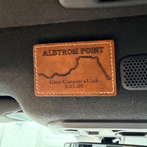 May include: A brown leather patch with the text "ALSTROM POINT" and a map outline. Below the map, it reads "Glen Canyon * Utah 5.01.26". The patch has white stitching around the edges.
