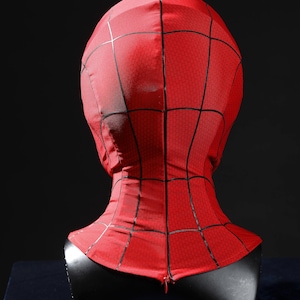 May include: A red fabric mask featuring a black web pattern across the entire surface. The mask covers the head and neck area, displaying a textured material with a visible zipper closure at the base of the neck, presented on a black display bust.