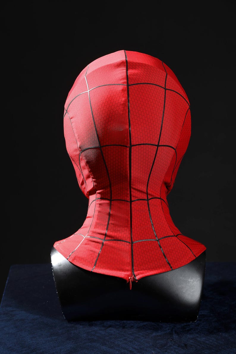 May include: A red fabric mask featuring a black web pattern across the entire surface. The mask covers the head and neck area, displaying a textured material with a visible zipper closure at the base of the neck, presented on a black display bust.