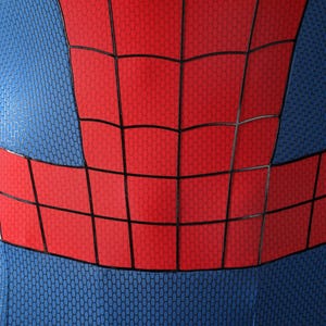 May include: A close-up of a blue and red bodysuit featuring a textured honeycomb pattern. The garment displays a prominent red chest and waist section overlaid with a black grid design, contrasting against the blue fabric on the sides.