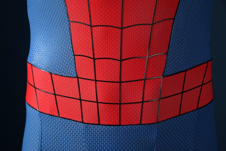 May include: A close-up of a blue and red bodysuit featuring a textured honeycomb pattern. The garment displays a prominent red chest and waist section overlaid with a black grid design, contrasting against the blue fabric on the sides.