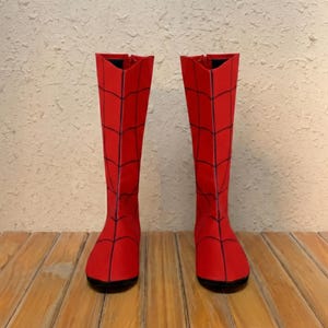 Puede incluir: Un par de botas hasta la rodilla de color rojo vibrante, con un patr&oacute;n de telara&ntilde;a negro prominente impreso en toda la superficie. Las botas tienen un dise&ntilde;o de ca&ntilde;a alta y estructurada con punta redondeada y suela plana.