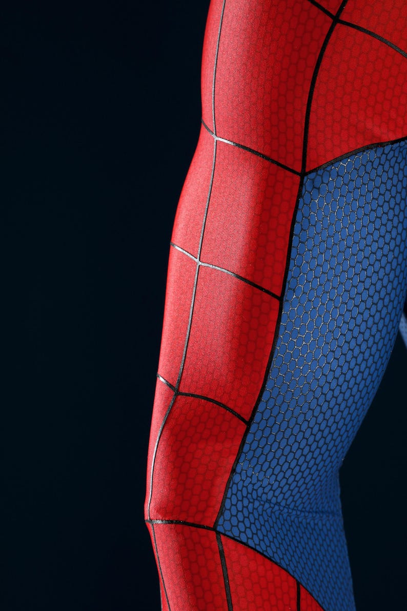 May include: A close-up view of a fabric garment featuring a vibrant red and blue color scheme. The red sections are adorned with a prominent black web pattern, while the blue sections display a subtle, repeating hexagonal texture throughout.