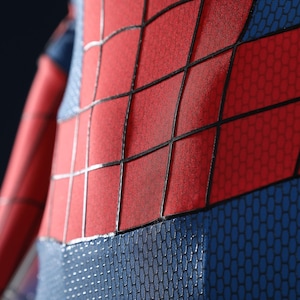 May include: A red and blue bodysuit featuring a textured honeycomb pattern on the blue sections and a prominent black grid design overlaid on the red panels. The fabric displays a distinct contrast between the smooth red and the textured blue.