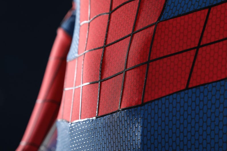 May include: A red and blue bodysuit featuring a textured honeycomb pattern on the blue sections and a prominent black grid design overlaid on the red panels. The fabric displays a distinct contrast between the smooth red and the textured blue.