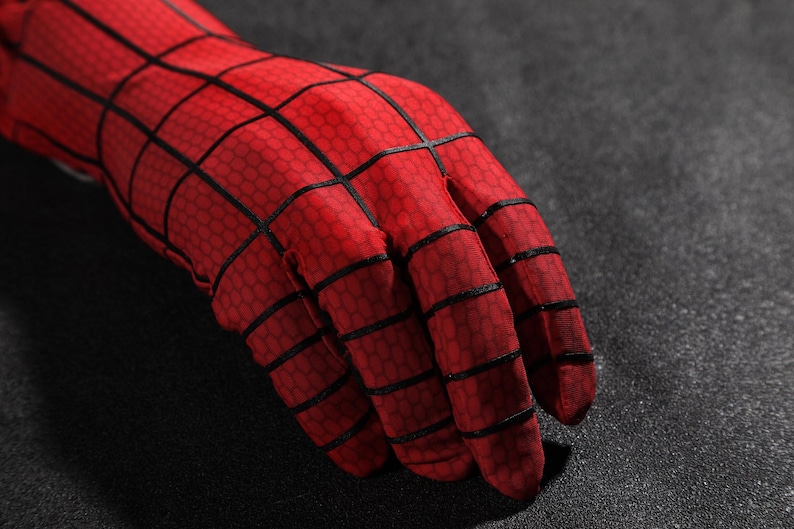 May include: A red fabric glove featuring a black grid pattern across the surface. The material has a subtle hexagonal texture throughout, and the black lines are raised, creating a distinct web-like design that covers the fingers and the wrist area.