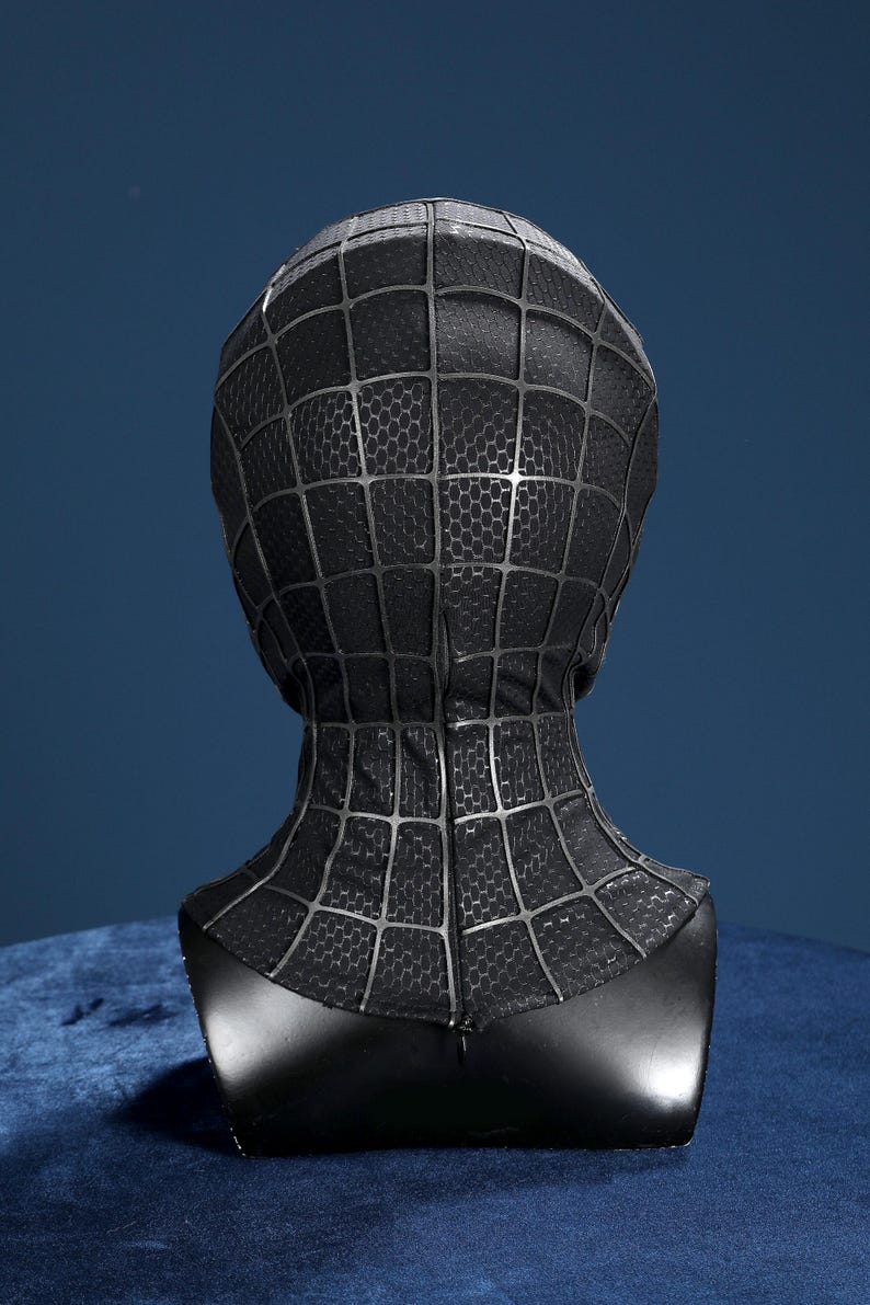 K&ouml;nnte beinhalten: Eine schwarze Vollkopfmaske mit einem erhabenen, dunkelgrauen Spinnennetz-Muster auf der gesamten Oberfl&auml;che. Der Stoff weist eine subtile hexagonale Textur auf und das Design umfasst eine vertikale Naht in der Mitte der R&uuml;ckseite.