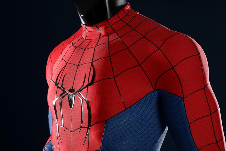 May include: A red and blue long-sleeve shirt featuring a black spider web pattern across the red chest and shoulder panels. A large, black, stylized spider emblem is centered on the chest. The fabric has a textured, honeycomb-like surface.