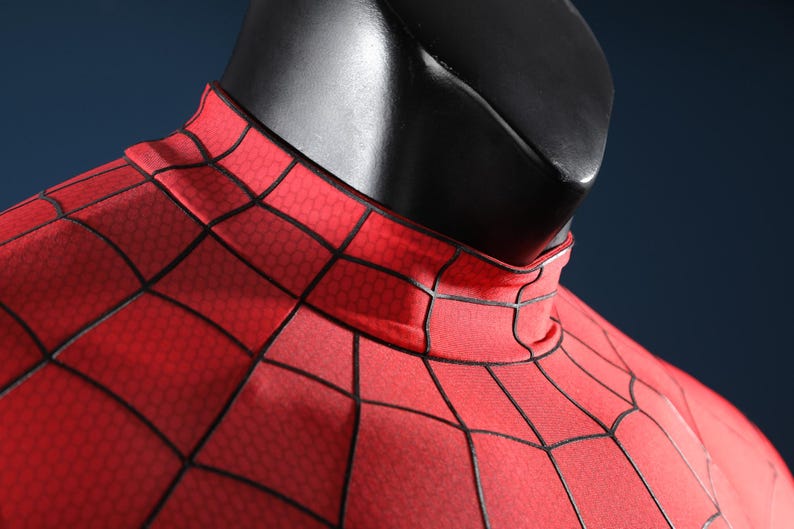 May include: A red fabric garment featuring a black web pattern with a high mock neck collar. The material displays a subtle hexagonal texture throughout the surface, worn on a black mannequin torso against a dark blue background.