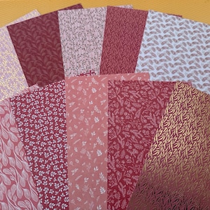 Peut inclure: Une collection de feuilles de papier à motifs dans diverses nuances de rouge, rose et or. Les motifs comprennent des motifs floraux et de feuilles, certains avec des accents dorés métalliques. Les papiers sont disposés en éventail sur un fond jaune.