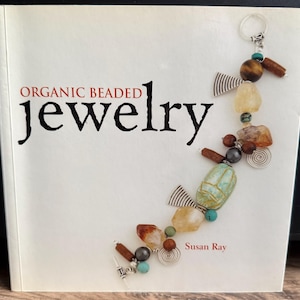Könnte beinhalten: Buchcover mit dem Titel "ORGANIC BEADED jewelry" in schwarzer und roter Schrift. Das Cover zeigt ein Perlen-Schmuck-Design mit verschiedenen Natursteinen und silbernen Akzenten. Der Name des Autors, Susan Ray, steht unten.