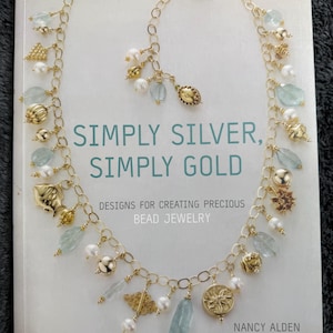Könnte beinhalten: Ein Buch mit dem Titel "SIMPLY SILVER, SIMPLY GOLD" mit Gold-Schmuck-Designs. Das Cover zeigt eine goldene Halskette mit blau-grünen Steinen, Perlen und goldenen Charms. Das Buch ist für die Herstellung von kostbarem Perlenschmuck.
