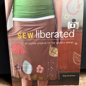 Könnte beinhalten: Das Buchcover zeigt den Titel "SEW liberated" in gelber und weißer Schrift. Das Cover zeigt einen braunen Rock mit bunten Stoffapplikationen. Das Buch handelt von 20 stilvollen Nähprojekten.