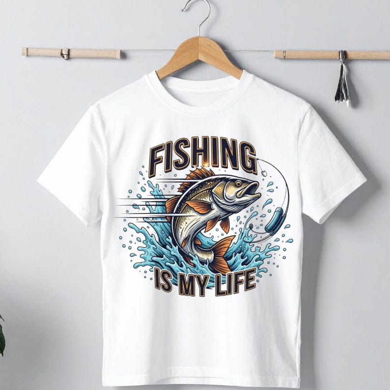 K&ouml;nnte beinhalten: Wei&szlig;es T-Shirt mit einem farbenfrohen Grafikdesign eines Fisches, der aus blauem Wasser springt, mit dem Schriftzug "FISHING IS MY LIFE". Das Design beinhaltet einen Angelhaken und eine Angelschnur, wodurch ein dynamisches und auff&auml;lliges Bild entsteht.