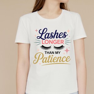 May include: White t-shirt with the text "Lashes Longer Than My Patience" in navy blue, gold, and pink. The design includes stylized eyelashes and stars. The shirt is a crew neck.