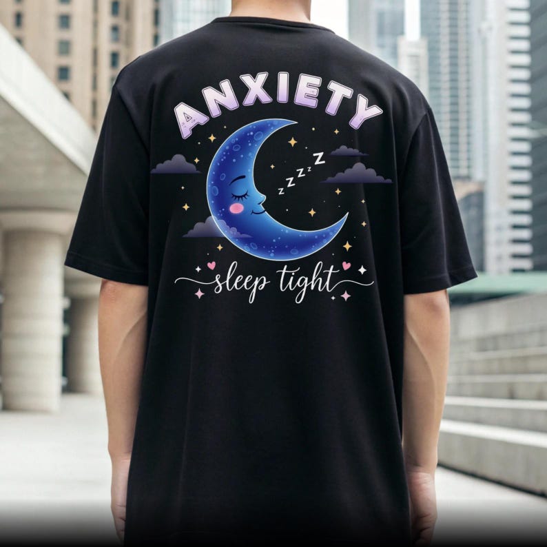 May include: Black t-shirt with a graphic on the back featuring a blue crescent moon with a sleeping face, stars, and the text "ANXIETY sleep tight". The text is in a light purple color.