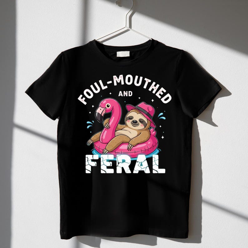 May include: Black t-shirt with a graphic of a sloth wearing a pink hat and floating on a pink flamingo pool float. The text on the shirt reads "FOUL-MOUTHED and FERAL".