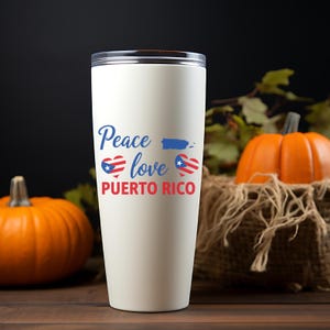以下が含まれることがあります： 「Peace love PUERTO RICO」の文字が青と赤で描かれた白いタンブラー。ハートと旗のグラフィックもあしらわれています。タンブラーは、カボチャと紅葉を背景に配置されています。