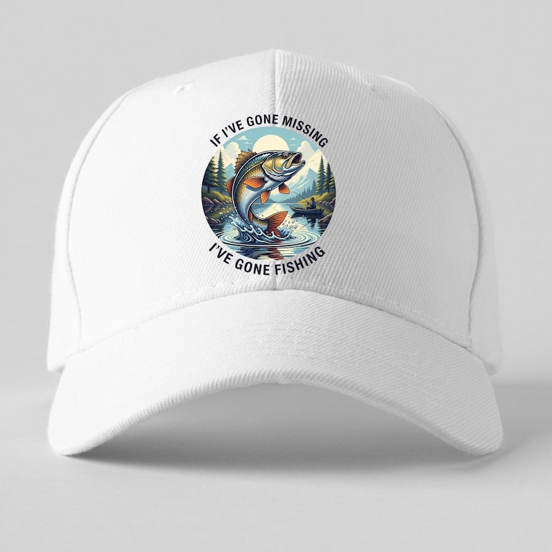 K&ouml;nnte beinhalten: Wei&szlig;e Baseballkappe mit einem kreisf&ouml;rmigen Motiv eines springenden Fisches in einer See-Szene. Der Aufdruck enth&auml;lt den Text "IF I'VE GONE MISSING I'VE GONE FISHING". Die Kappe besteht aus strapazierf&auml;higem Stoff.
