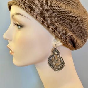 May include: Silver filigree earrings with a white bead accent. The earrings are dangling and have a circular shape.