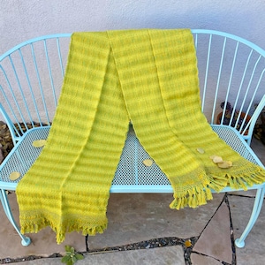 Peut inclure: Un châle tissé vert lime avec des franges sur un banc en métal bleu. Le châle est plié en deux et présente un motif rayé.