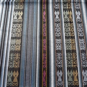 May include: A close-up of a woven fabric with a striped pattern. The fabric is black, white, blue, and gold with geometric designs.