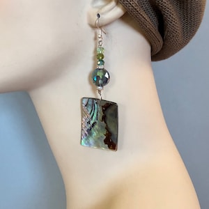 Peut inclure: Boucles d'oreilles en forme de coquille d'ormeau iridescentes vertes et bleues avec un crochet argenté et une perle de cristal.