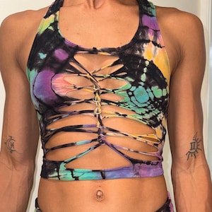 May include: A tie-dye halter top in a vibrant mix of colors including black, purple, yellow, and teal. The top features a unique design with cut-out sections and a laced-up front. The garment is a crop top style, suitable for activewear or casual wear.