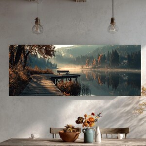 May include: A panoramic canvas print showing a tranquil lake scene. A wooden jetty extends into the calm water, with a bench at the end. The surrounding landscape features trees with autumn colours, and a misty atmosphere.