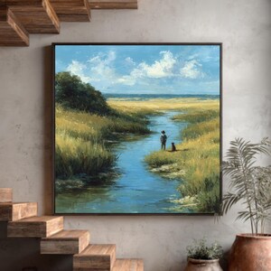 Pode incluir: Uma pintura de paisagem emoldurada retrata uma serena cena de pântano. Uma figura com um cão está perto de uma via navegável azul, rodeada por ervas altas e sob um céu nublado. A obra de arte é exibida em uma parede de tons neutros.