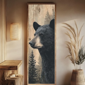 Peut inclure: Impression artistique verticale encadrée représentant le profil d'un ours noir devant une forêt. L'œuvre est posée sur un fond de planches de bois, avec un cadre en bois naturel. Le pelage de l'ours est détaillé, et la forêt est dans des tons sourds.