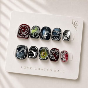 以下が含まれることがあります： LOVE COATED NAILと記された白い台紙に並べられた10枚のネイルチップ。深みのある赤の渦巻き模様、メタリックシルバーのアクセント、ダークブルーのグラデーション、シルバーの立体的な装飾が施された黄緑色の中心部など、多様なデザインが特徴です。