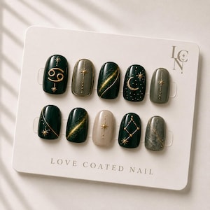 Peut inclure: Un ensemble de dix faux ongles sur une carte de présentation marquée LOVE COATED NAIL et LCN. Les ongles présentent des tons vert foncé, gris et beige avec des motifs célestes dorés, incluant des étoiles, une lune et le signe du Cancer.