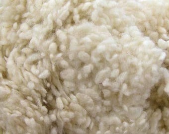 May include: Close-up of a cream-colored, textured wool fleece. The fibers are tightly packed and appear soft and fluffy, with a slightly uneven surface. The wool has a natural, undyed appearance.