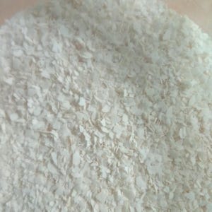 Pode incluir: Close-up de uma pilha de flocos brancos de formato irregular. Os flocos são de uma cor branca clara e estão densamente compactados. A textura dos flocos é áspera e irregular, sugerindo um material natural ou processado.