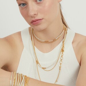 May include: Layered gold and white beaded necklaces with a chain link pendant