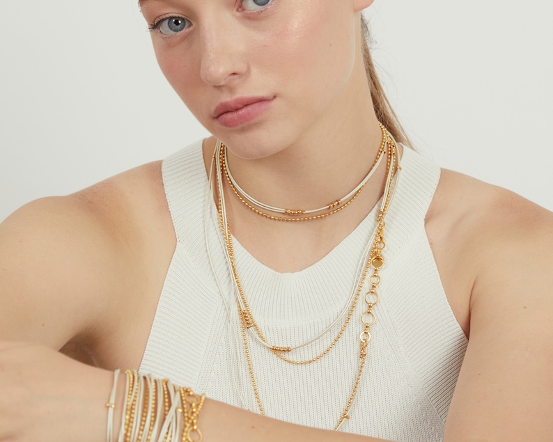 May include: Layered gold and white beaded necklaces with a chain link pendant