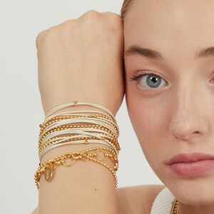 May include: A stack of gold and white bracelets with a gold charm
